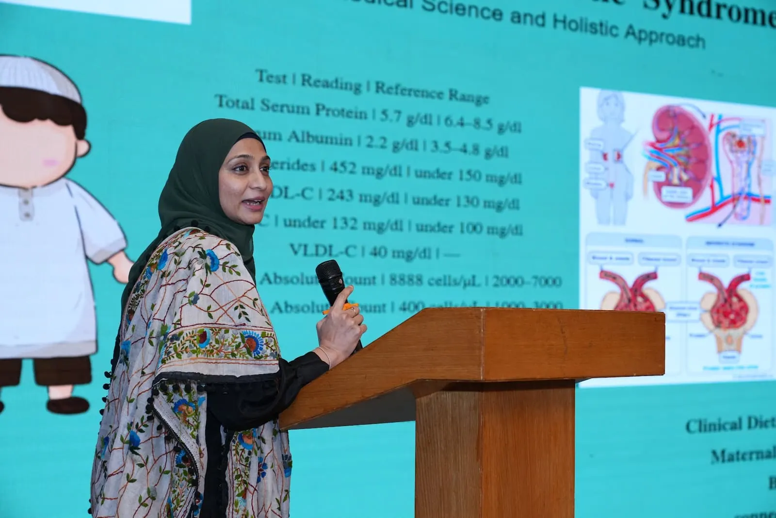 A coach presenting a nephrotic syndrome case at HolistiCon 2025, the slide behind her showing the laboratory panel against reference ranges
